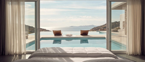 Luxuriöses Hotelzimmer mit hochwertigem Bett und gestepptem Topper vor bodentiefen Fenstern, mit Blick auf einen Infinity-Pool und das Meer – inspiriert von exklusivem Schlafkomfort in Luxushotels.