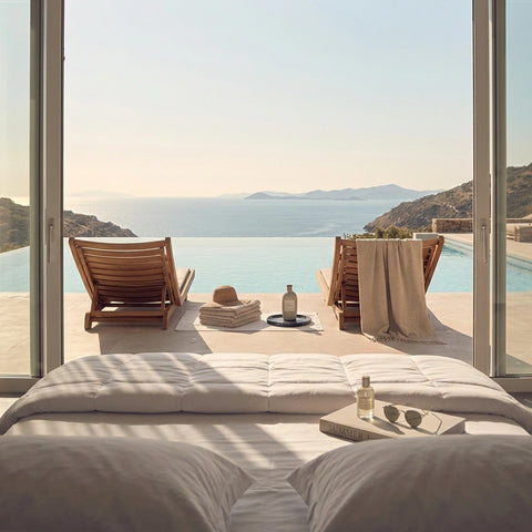 Helles Schlafzimmer mit Bett und Meerblick auf einen Infinity-Pool – sommerliche Atmosphäre für erholsamen Schlaf und Entspannung.