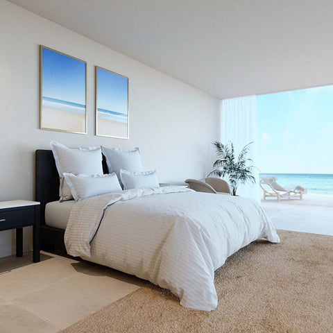 Ein großes, einladendes Doppelbett bezogen mit eleganter, weißer Microstripe Bettwäsche und mehreren Kissen in einem minimalistischen Schlafzimmer mit offener Fensterfront zum Meer