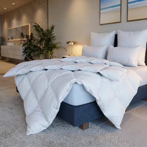 Elegantes Bett mit weißer Premium-Bettwäsche, mehreren Kissen und voluminöser Bettdecke in hochwertiger Hoteloptik.