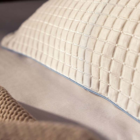 Nahaufnahme eines Kühlkissenbezugs mit strukturierter Oberfläche und feiner blauer Biese auf einem Bett, für ein angenehm frisches Schlafgefühl.