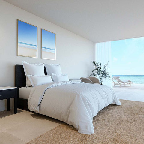 Ein weiches, weißes Bett-Set mit Premium Bettdeckenbezug und passenden Kissen in einem hellen, minimalistischen Schlafzimmer mit Meerblick und moderner Kunst an der Wand.