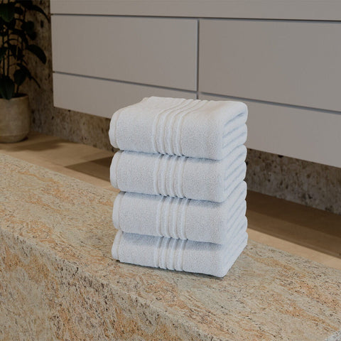 Premium Luxushotel-Handtücher 4er Set mit vier sauber gefalteten weißen Handtüchern auf einer Natursteinablage in einem modernen Badezimmer.