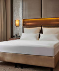Ein ordentlich gemachtes Doppelbett in einem luxuriösen Hotelzimmer, bezogen mit einem glatten, weißen Premium-Spannbettlaken unter warm beleuchteten Wandlampen und stilvollem Kopfteil.