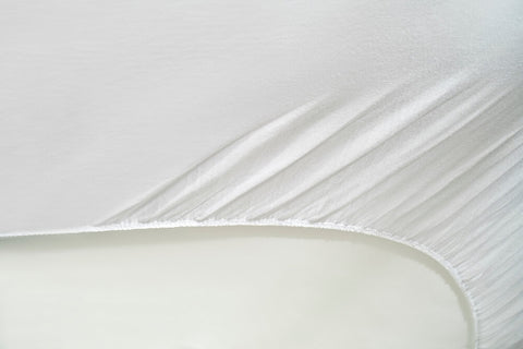 Nahaufnahme der elastischen Ecke eines weißen Premium-Spannbettlakens mit strapazierfähigem Rundumgummizug, der sich flexibel und faltenfrei um eine Matratze spannt.